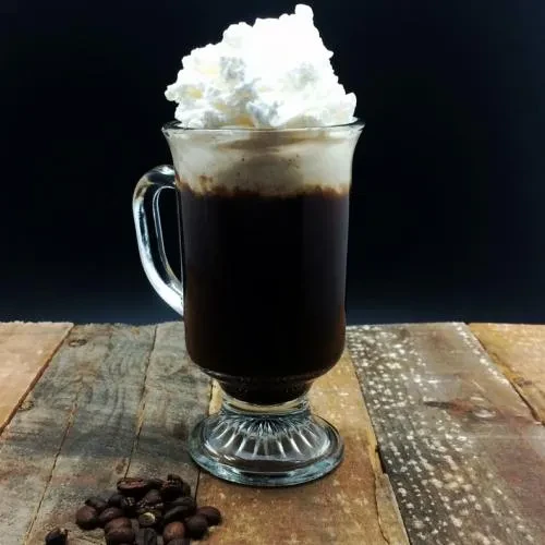Glass mug of coffee with whipped cream on wood, coffee beans.