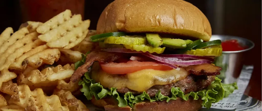 Close-up of a burger with avocado, bacon, cheese, and waffle fries.