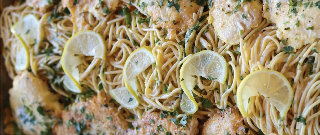 Creamy pasta dish with breaded chicken/fish, lemon slices, and green herbs.
