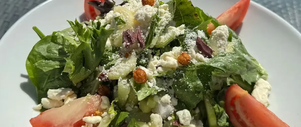 Vibrant salad close-up: greens, feta, tomatoes, olives, and crunchy elements.