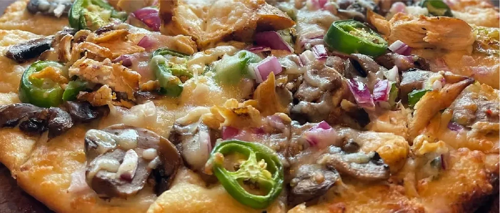 Close-up pizza with melted cheese, jalapeños, mushrooms, onions, and crispy pieces.