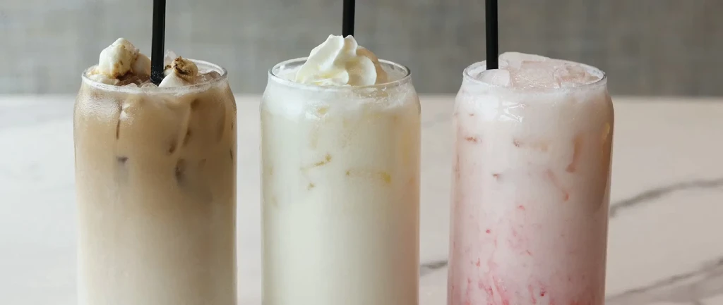 Side-by-side iced coffee, milkshake, and pink fruit drink with straws.