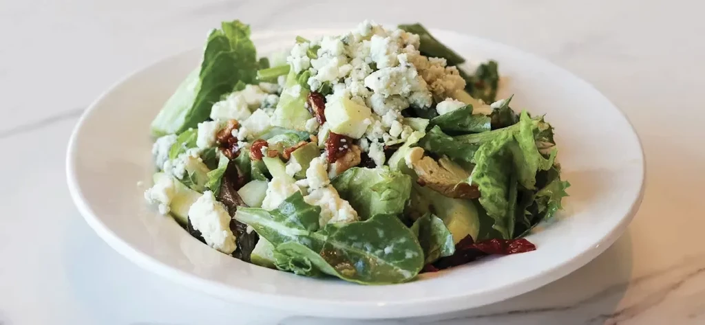 Green leafy salad with blue cheese, red and light chunks.