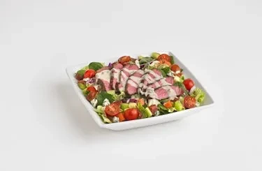 Grilled steak salad with greens, tomatoes, and cheese in a white bowl.