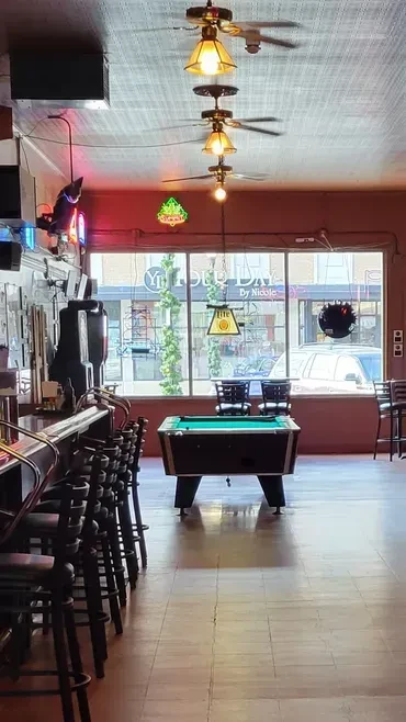 Empty bar interior with long counter, pool table, and street windows.