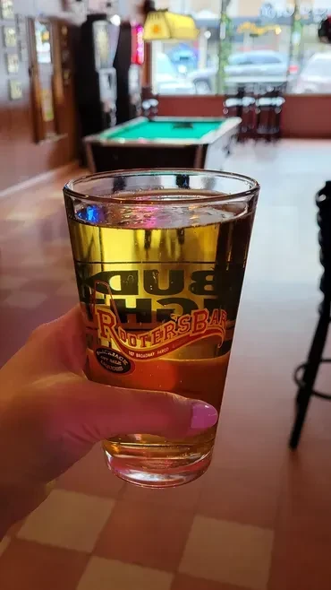 Hand holding Bud Light beer in Rooters Bar with pool table.