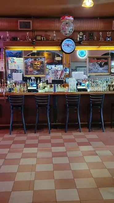 Well-stocked traditional bar counter with taps, bottles, and stools.