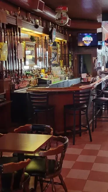 Cozy traditional bar interior with a well-stocked counter and checkered floor.