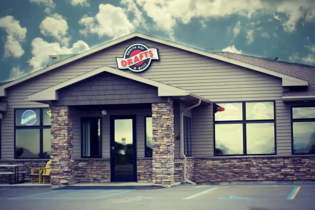 Drafts Sports Bar & Grill exterior, light brown siding, stone, yellow chairs.