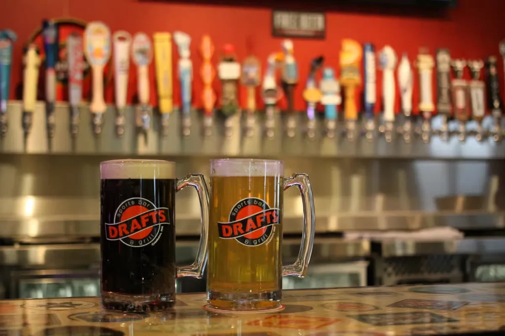 Two DRAFTS beer mugs, dark and light, on a bar counter.