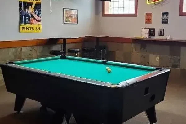 Pub interior with green pool table, high-top seating, and windows.