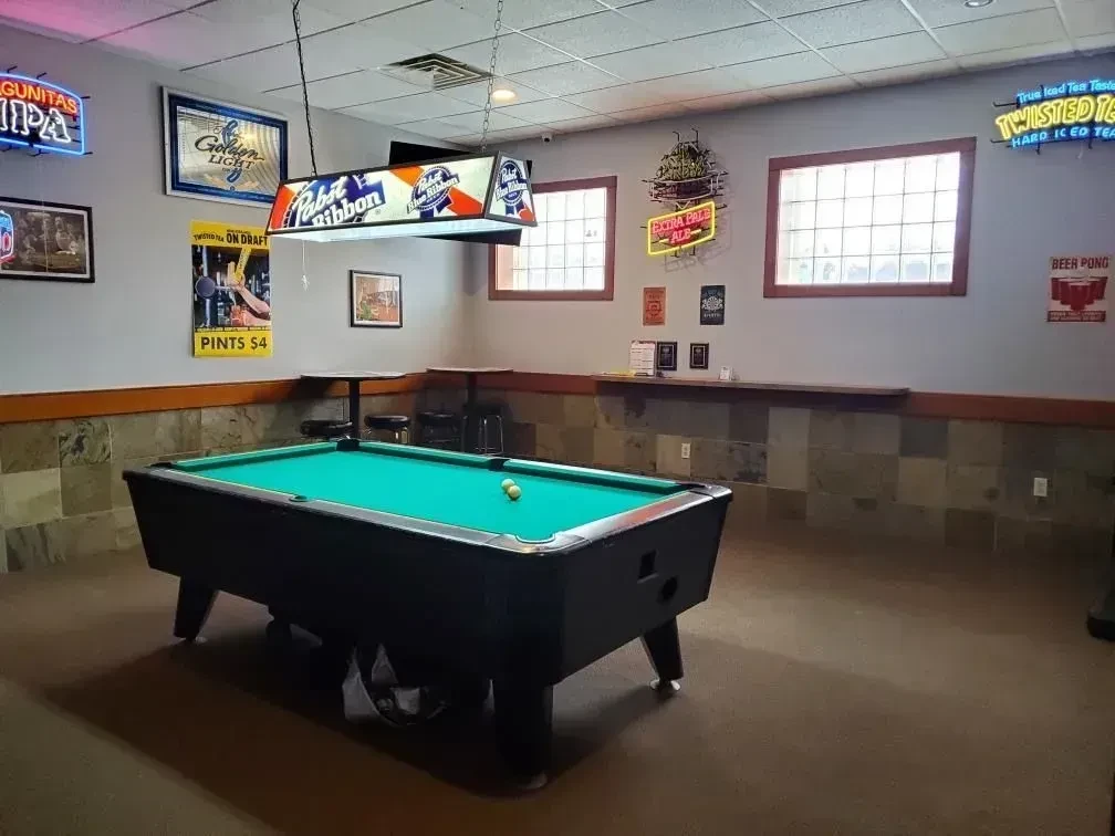 Green pool table with yellow balls in a bar with neon signs.