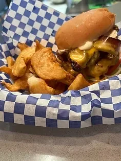 Cheeseburger with toppings and wedge fries served in a checkered basket.