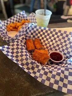 Two baskets of fried egg rolls, tater tots, and dipping sauces.