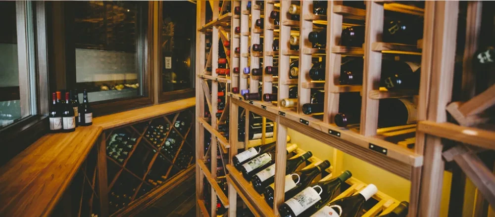 Rows of red wine bottles stored in a warm, well-lit wooden cellar.