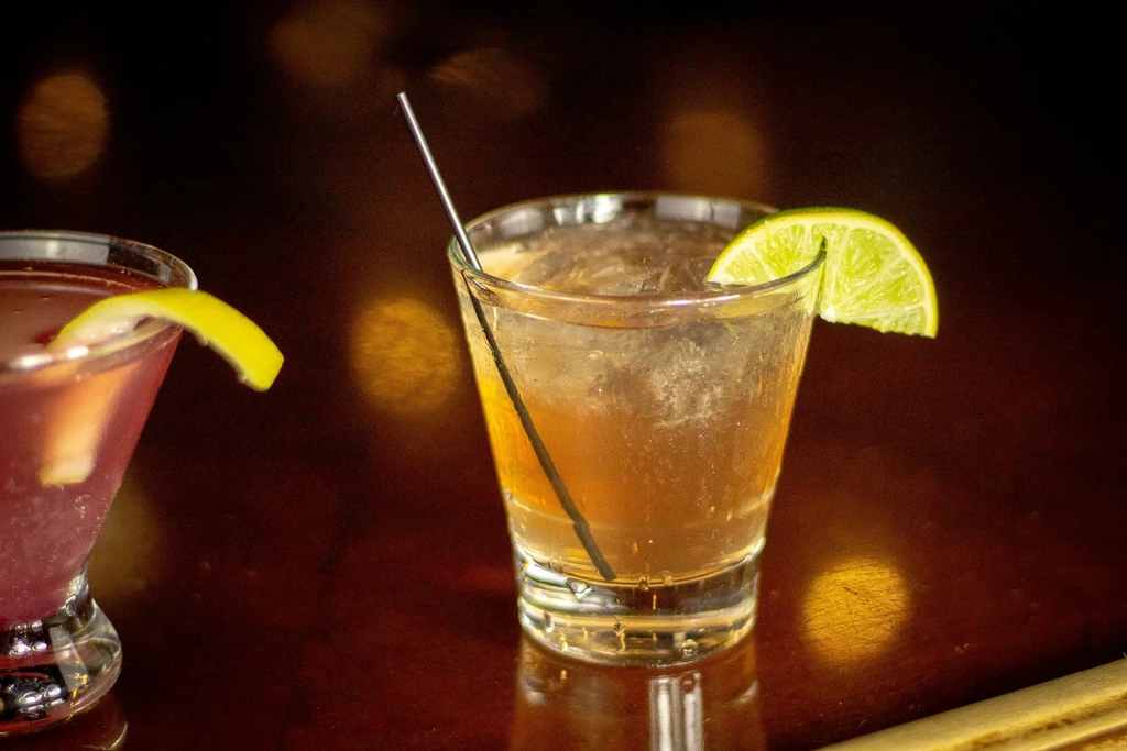 Amber cocktail with lime, pink cocktail on a dark bar.