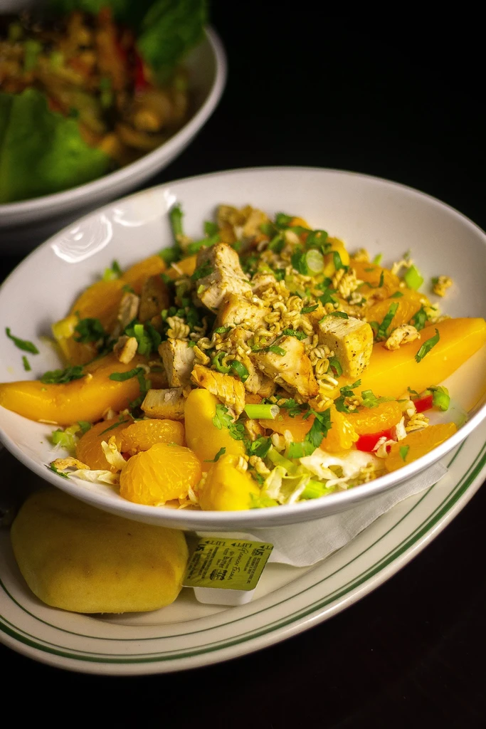 Colorful grilled chicken, fruit, and greens salad with crunchy topping.