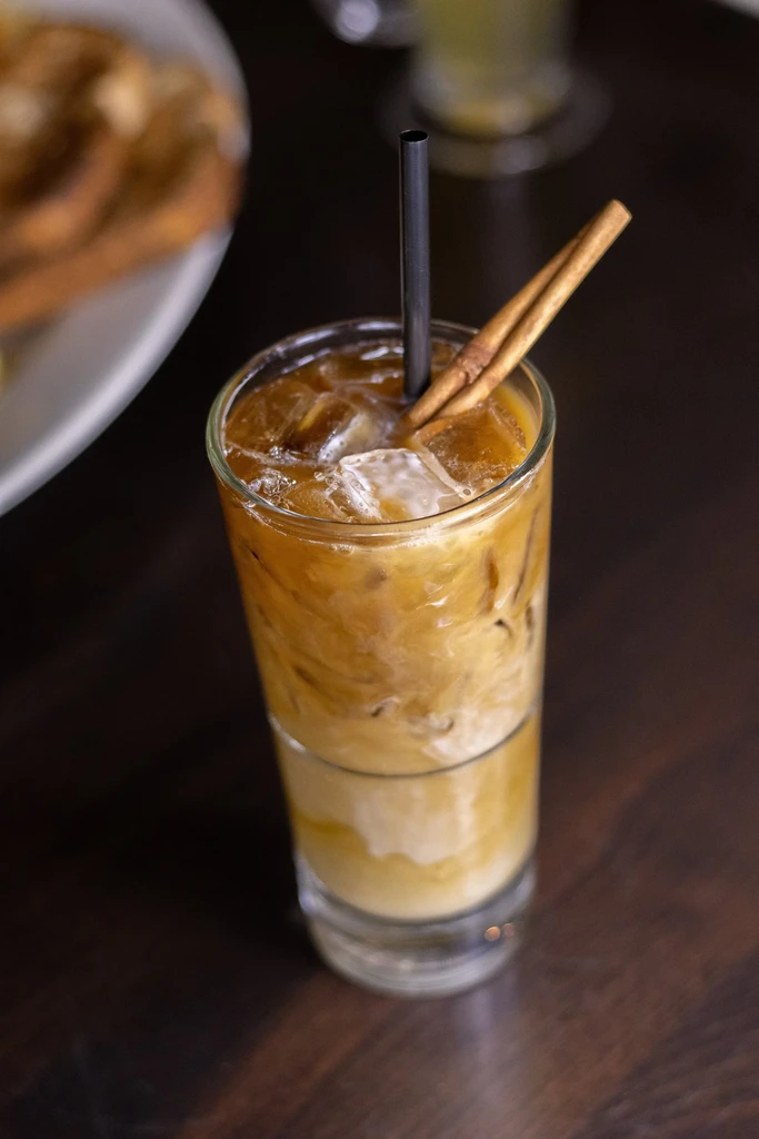 Layered iced coffee with ice, straw, and cinnamon sticks.