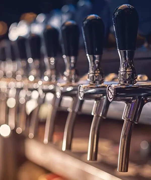 Close-up of shiny chrome beer taps, one sharply focused in a bar.