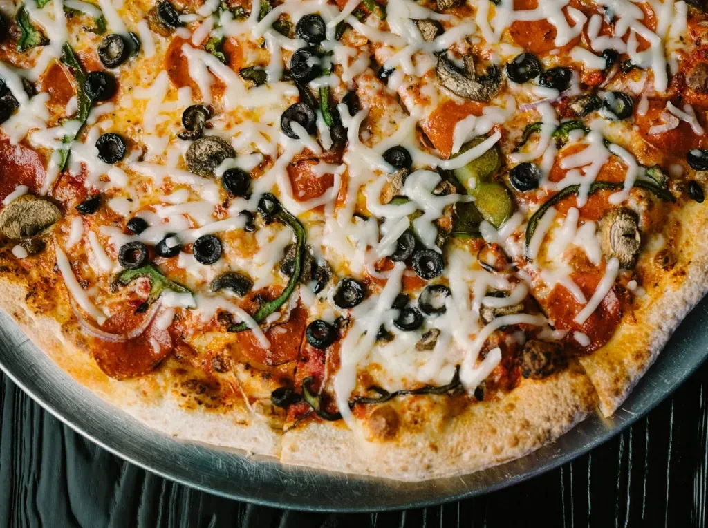 Freshly baked pizza topped with pepperoni, olives, bell peppers, and mushrooms.