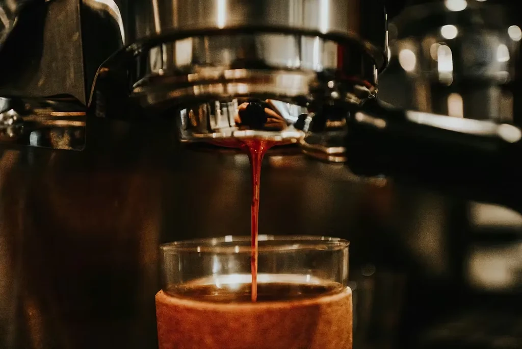 Close-up of espresso machine extracting dark red coffee into a glass.