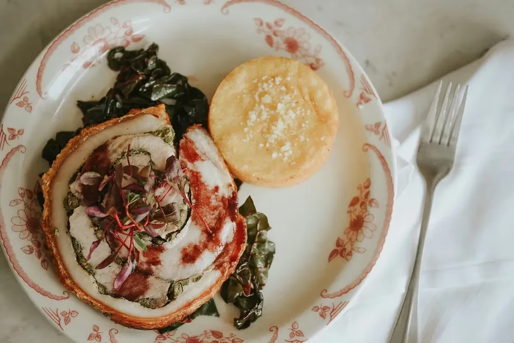 Crispy rolled meat, polenta, and greens on a floral plate with fork.