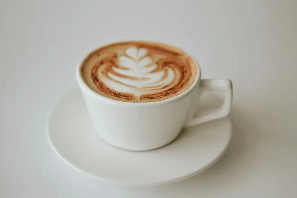 White ceramic cup with intricate leaf latte art on saucer.