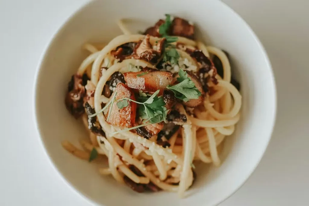 Bucatini pasta with crispy bacon, sautéed mushrooms, cheese, and parsley.