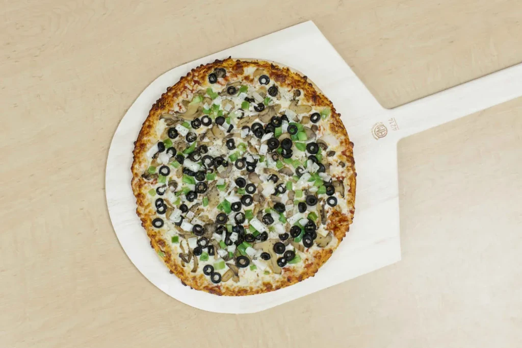 Baked pizza topped with peppers, olives, mushrooms on a wooden peel.