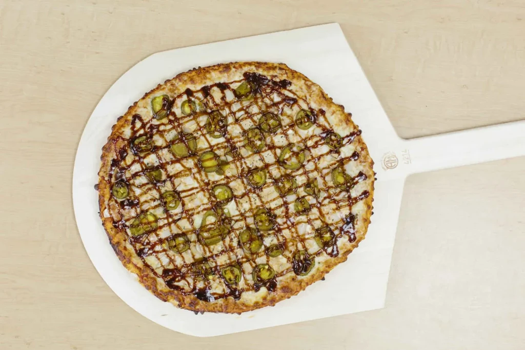 Pizza topped with jalapeños and drizzled dark sauce on a white peel.
