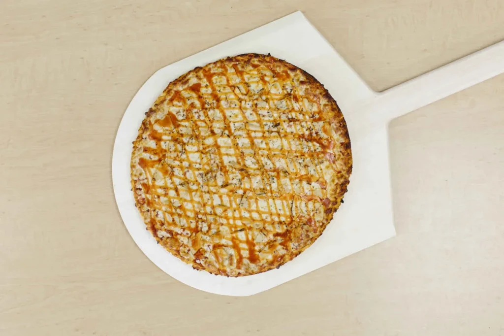 Round pizza with golden crust and crisscross sauce on a white peel.