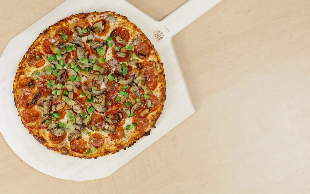 Freshly baked pizza with pepperoni, mushrooms, and bell peppers on a white peel.
