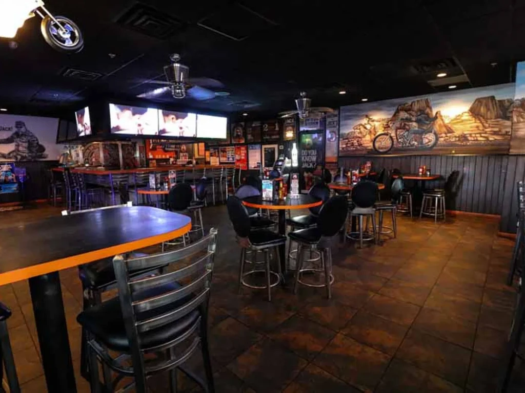 Dark, biker-themed bar interior with orange tables and motorcycle decor.