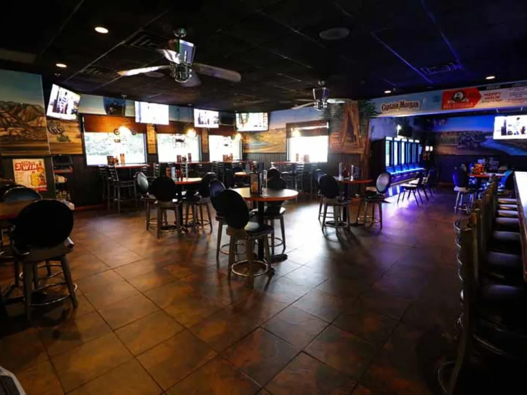 Empty, dimly lit sports bar interior with tables, TVs, and gaming machines.