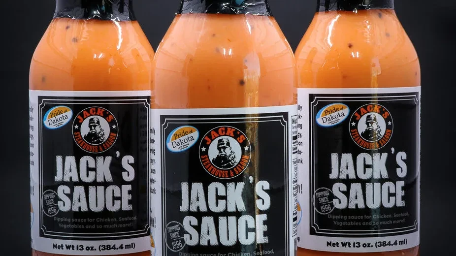 Three identical bottles of creamy orange Jack's Sauce with speckles.
