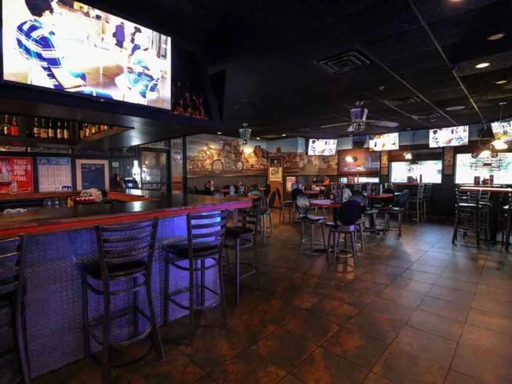 Dimly lit sports bar interior with blue-lit bar, multiple TVs, and murals.