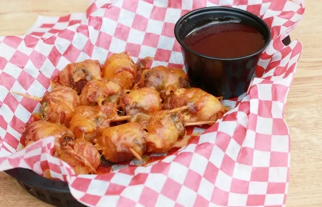 Basket of glazed golden-brown toothpick appetizers and dark dipping sauce.