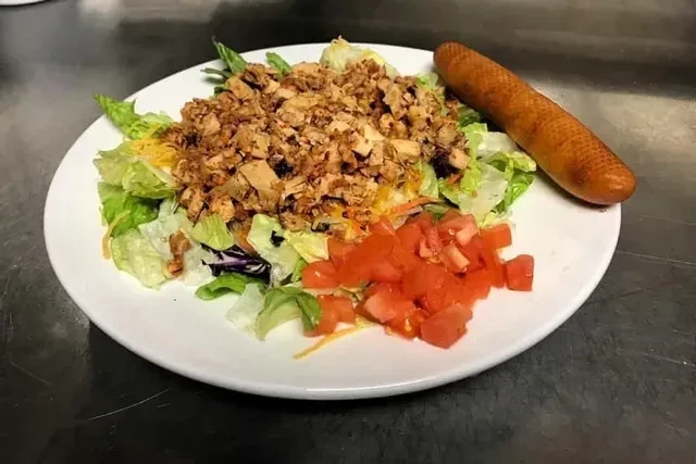 Plate of lettuce salad with meat, cheese, tomatoes, and a taquito.