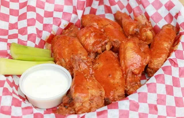 Buffalo chicken wings, celery, and dipping sauce in a checkered basket.