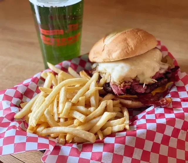 Loaded burger, crispy fries, and green drink in a checkered basket.