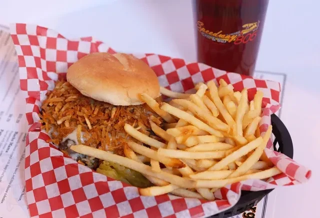 A burger topped with crispy onions, french fries, and pickles in a basket.