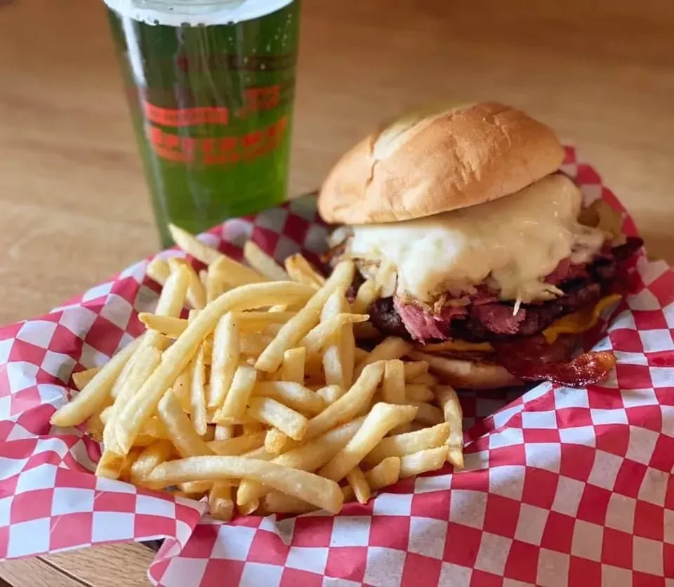 Burger with melted cheese, pastrami, and fries in a basket.