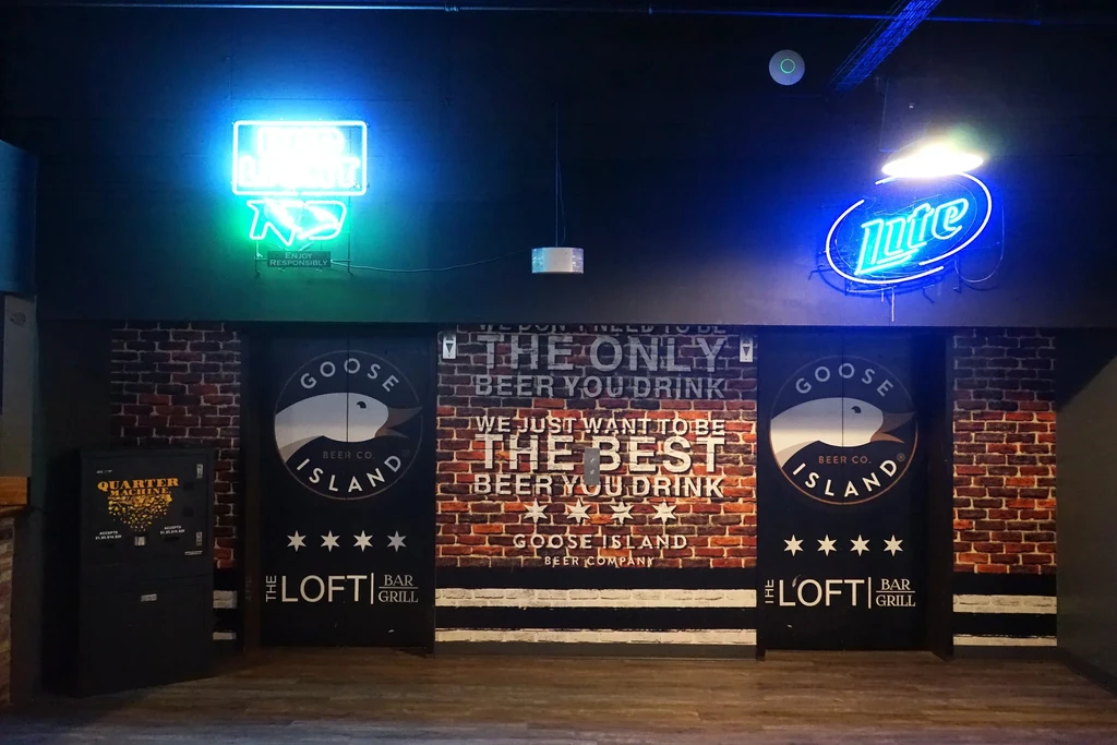 Bar interior with beer branding, neon signs, and brick walls.
