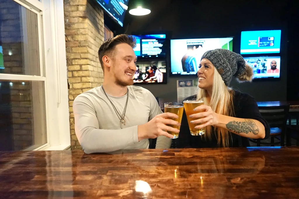 Smiling man and woman toasting beer glasses at a bar.
