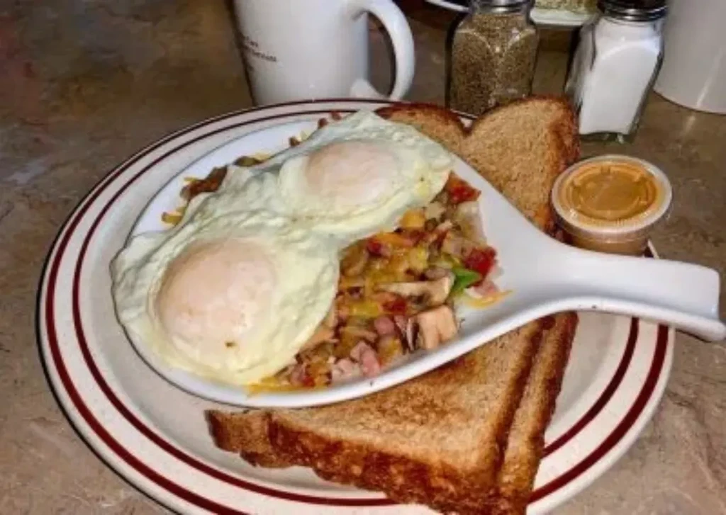 Close-up of fried eggs, hash, toast, and condiment on a diner plate.