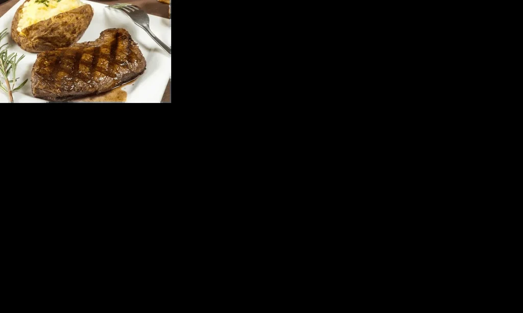Grilled steak with baked potato, butter, sour cream, and chives.