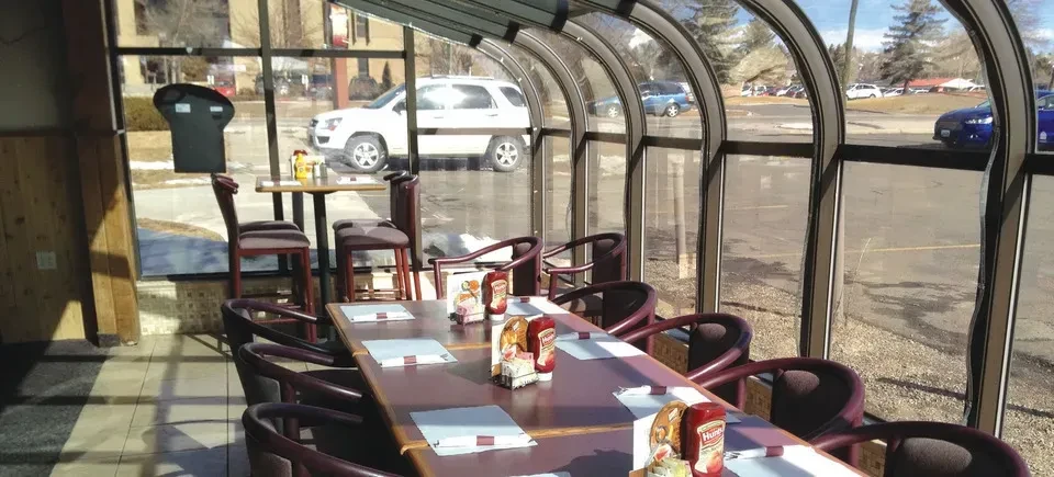 Bright, empty restaurant sunroom featuring a long table and glass roof.