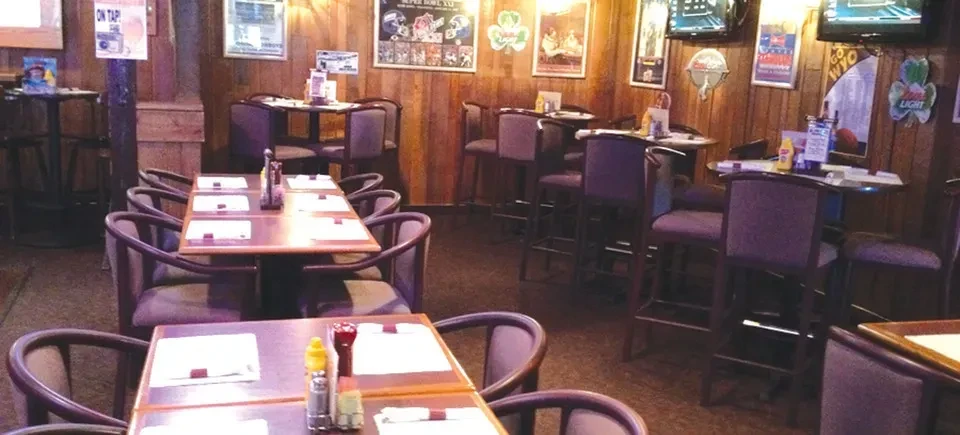 Dim, empty bar interior with wood paneling, purple seating, and sports decor.