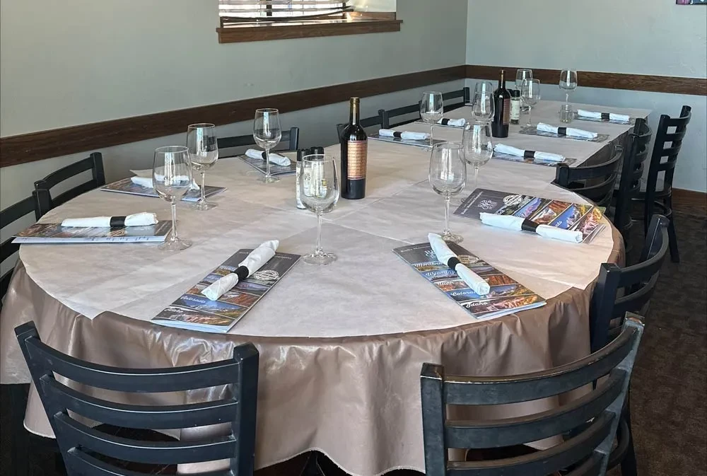 Empty restaurant dining room with set tables, wine glasses, and bottles.