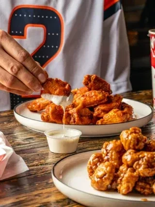 Two plates of chicken wings, one buffalo wing being dipped.